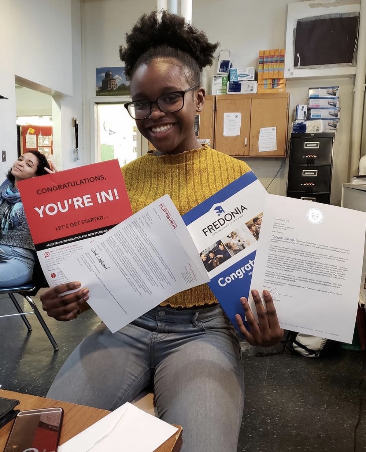DeWitt Clinton student proudly holding college acceptance letters, smiling beside a classmate